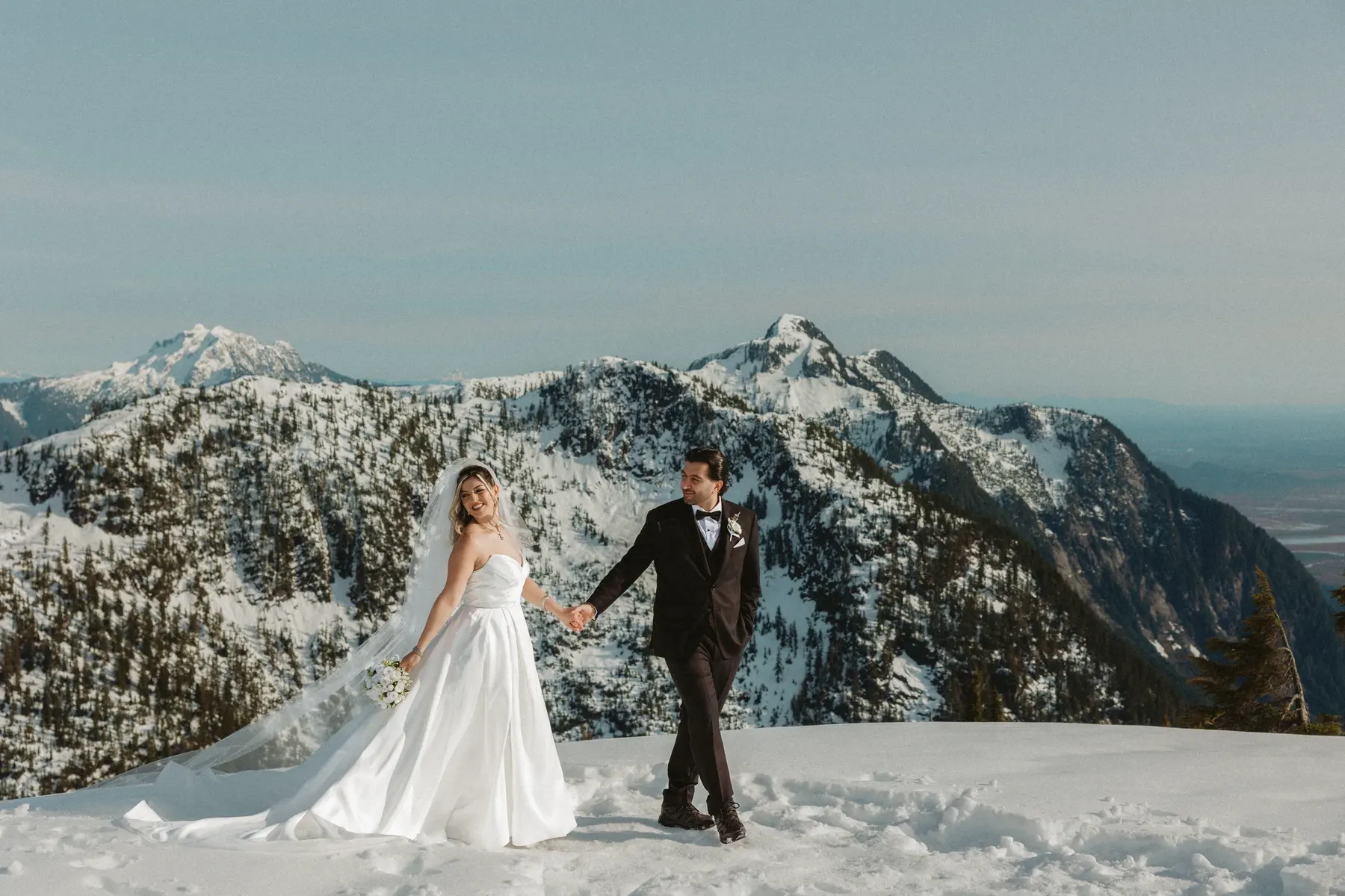 Couple walking hand in hand across a snowy mountain summit