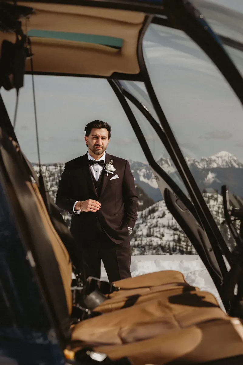 Groom standing in a helicopter doorway above the mountains
