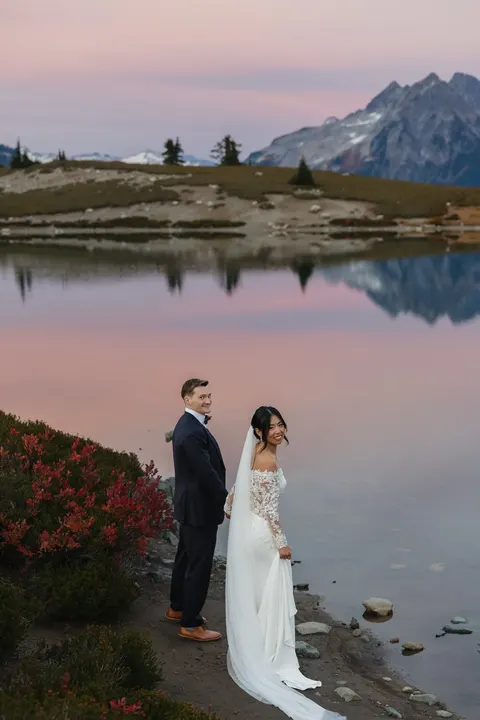 Newlyweds by an alpine lake under a pink sunset sky
