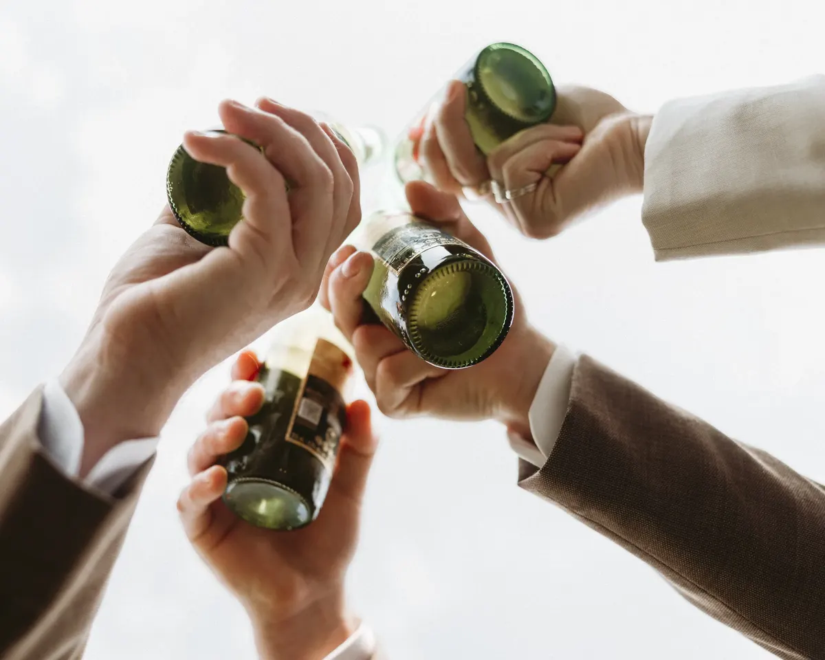 Friends clinking beer bottles together against the sky