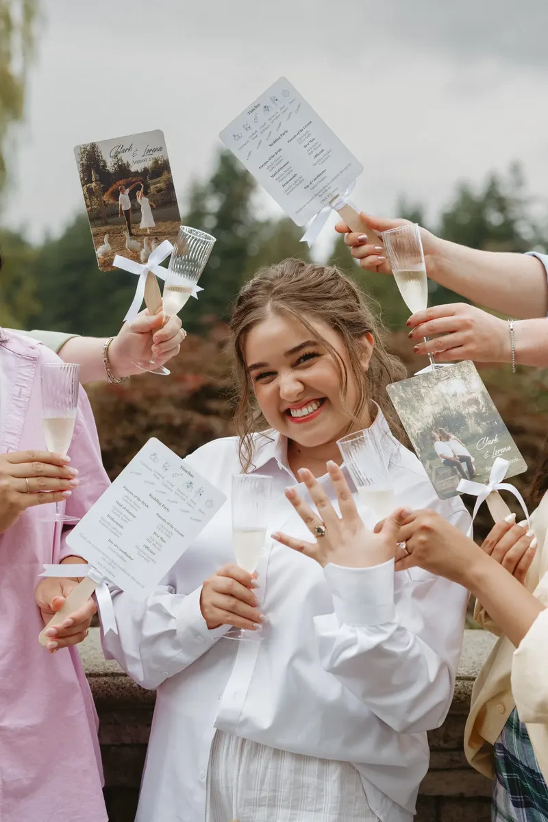 Bride laughing as her friends cheer and wave wedding programs around her