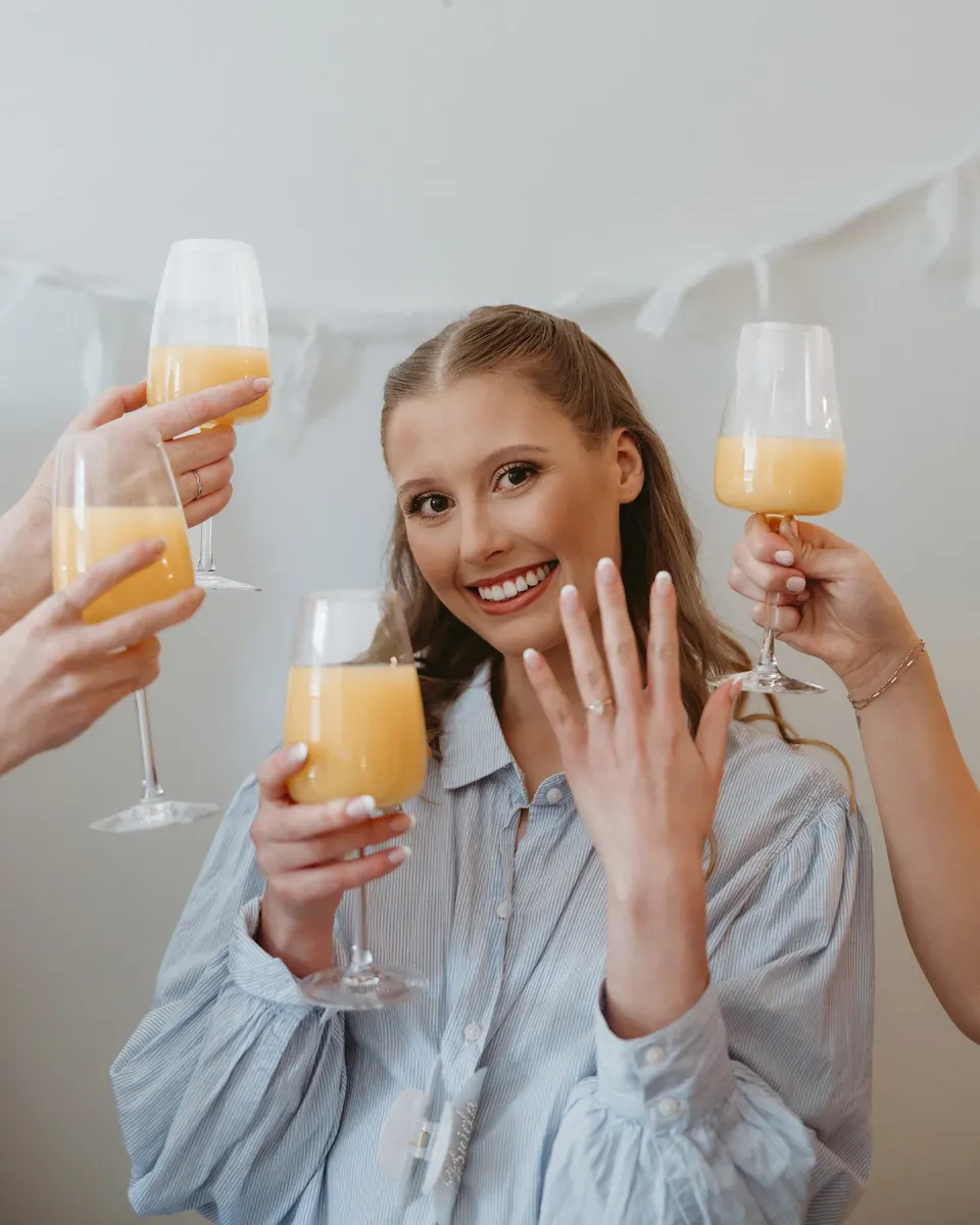 Bride showing off her ring as her friends toast with mimosas