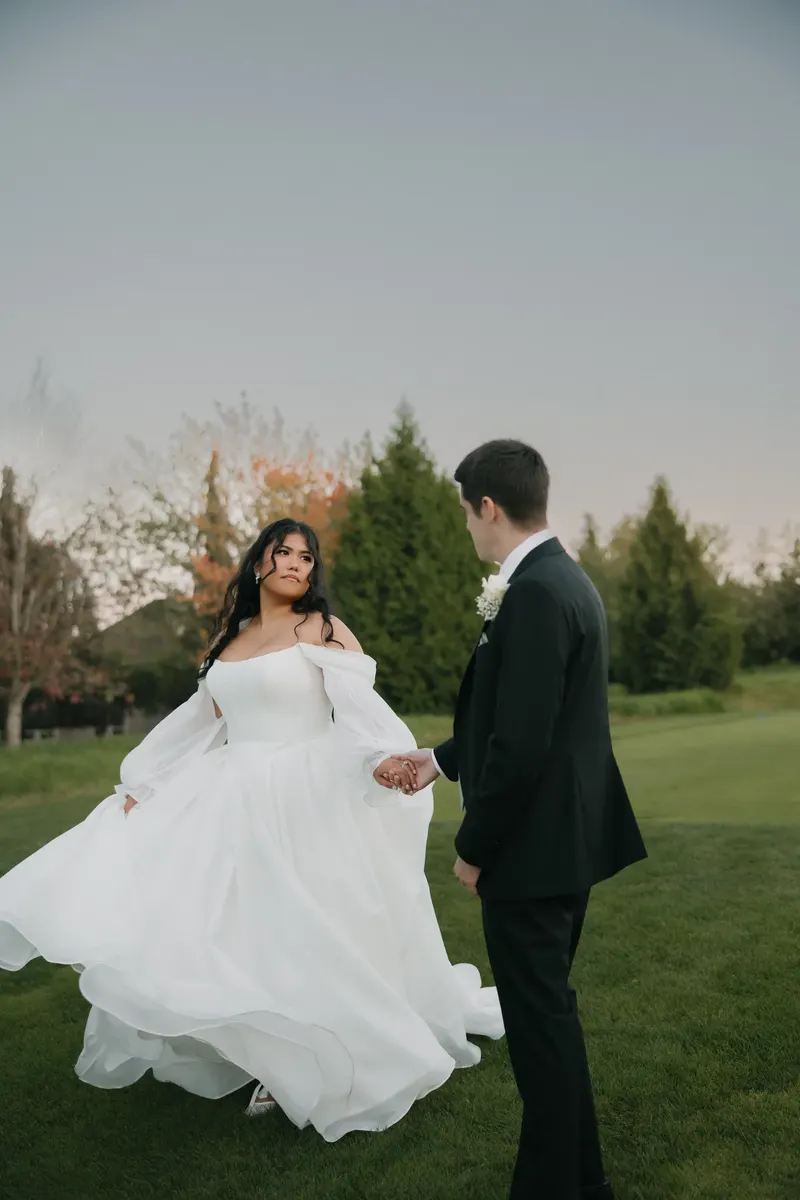 Bride twirling her full skirt as the groom watches
