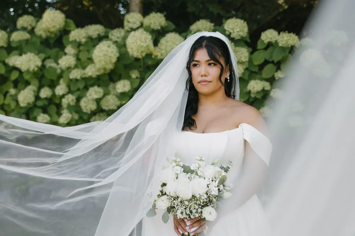 Bride in a sweeping veil in front of white hydrangeas