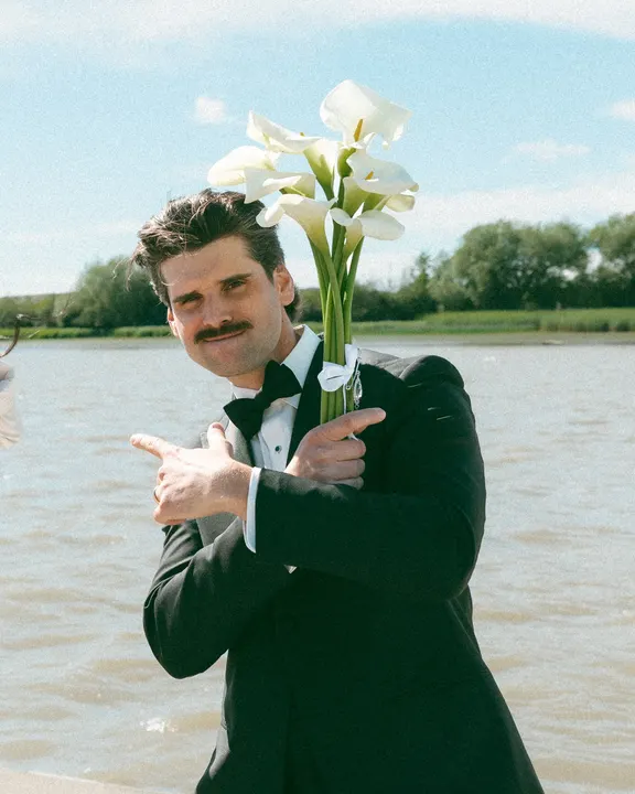Groom holding calla lilies and pointing finger guns at the camera